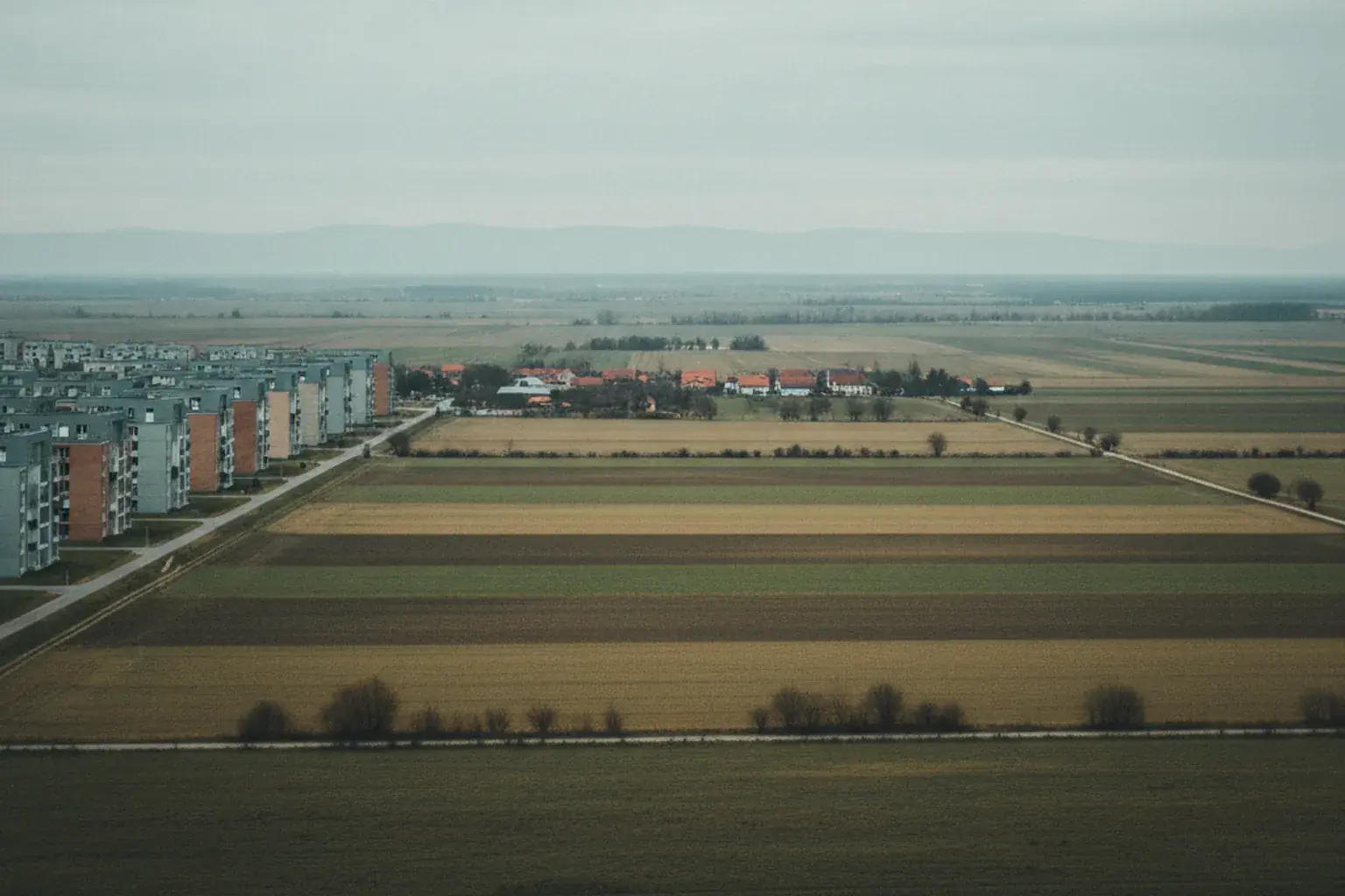 Blick von einer Anhöhe auf den Rand einer Stadt, wo Wohnblocks in Felder und einen Ortsrand übergehen