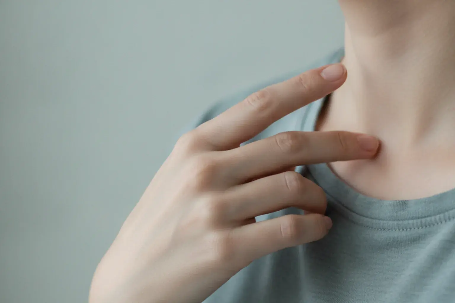 Nahaufnahme einer Hand, die mit zwei Fingerspitzen leicht auf den Bereich unter dem Schlüsselbein klopft